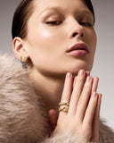 Close-up of a woman wearing gold earrings and rings with a neutral background