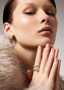 Close-up of a woman wearing gold earrings and rings with a neutral background