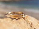 Three gold bracelets stacked on a rock with a blurred natural background