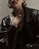 Woman wearing a black leather jacket with a gold ring on a neutral background