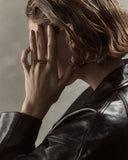 Woman wearing a black leather jacket and a gold ring with a neutral background