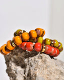 Three beaded bracelets in orange, red, and green on a rock with a light gray background