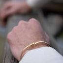 Close-up of a hand wearing a gold bracelet with a blurred background