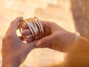 Woman holding a collection of gold bracelets against a warm, blurred background