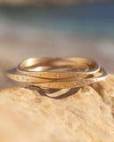 Three gold bracelets stacked on a rock with a blurred natural background