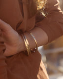 Close-up of a wrist wearing gold bangles on a blurred background