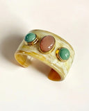 Wide gold natural horn cuff bracelet with three colored stones on a light background