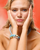 Woman wearing a blue beaded necklace and bracelets against a red background