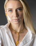 Woman wearing a gold chain necklace with a yellow pendant against a dark background