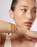 Woman wearing a large gold bangle bracelet on a plain background