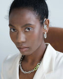 Woman wearing a white outfit with a necklace and earrings against a plain background