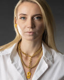 Woman wearing a white shirt and gold chain necklace with a yellow pendant against a dark background