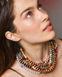 Woman wearing colorful layered beaded necklaces against a neutral background
