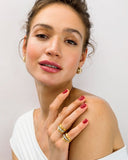 Woman wearing gold earrings and rings  against a plain background