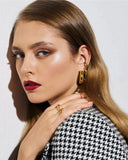 Woman wearing gold hoop earrings and rings with a neutral background